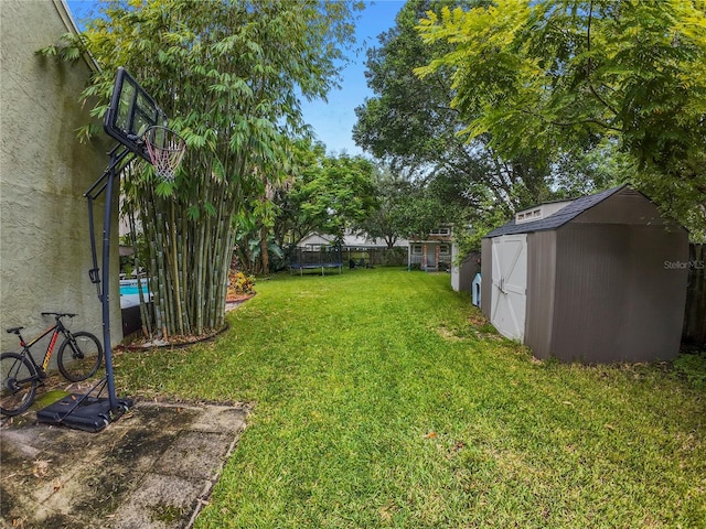 view of yard featuring an outbuilding, a shed, a trampoline, and fence