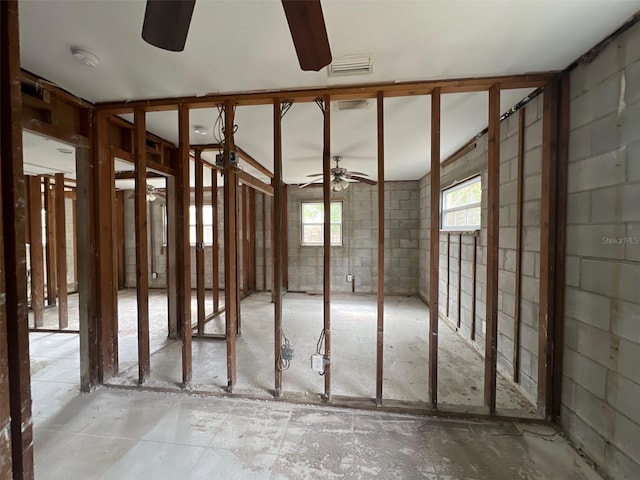 misc room featuring concrete block wall, visible vents, and a ceiling fan