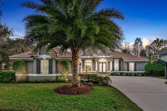 view of front facade featuring concrete driveway, a lawn, french doors, and stucco siding