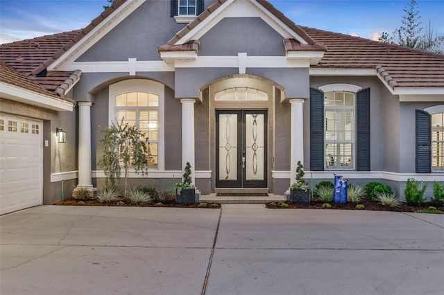 property entrance featuring french doors, a tiled roof, an attached garage, and stucco siding