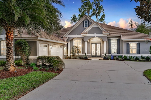 view of front of property featuring french doors, stucco siding, covered porch, an attached garage, and driveway