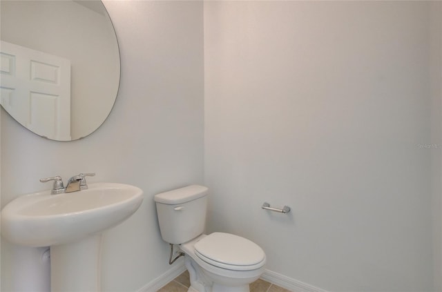 half bathroom with a sink, tile patterned flooring, toilet, and baseboards