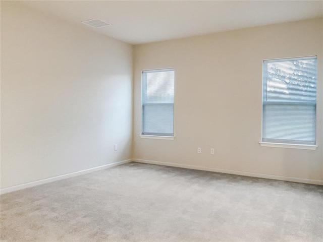 carpeted empty room featuring a healthy amount of sunlight, visible vents, and baseboards