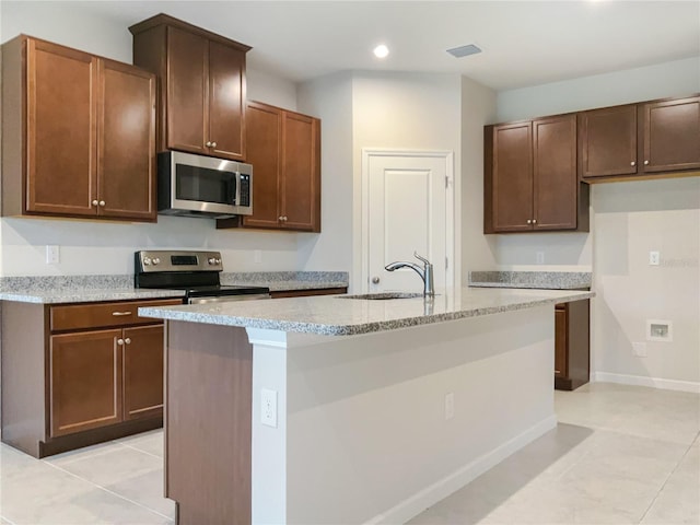 kitchen featuring a sink, visible vents, baseboards, appliances with stainless steel finishes, and a center island with sink