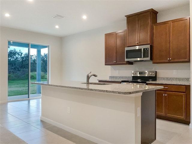 kitchen with an island with sink, light stone countertops, stainless steel appliances, a sink, and recessed lighting