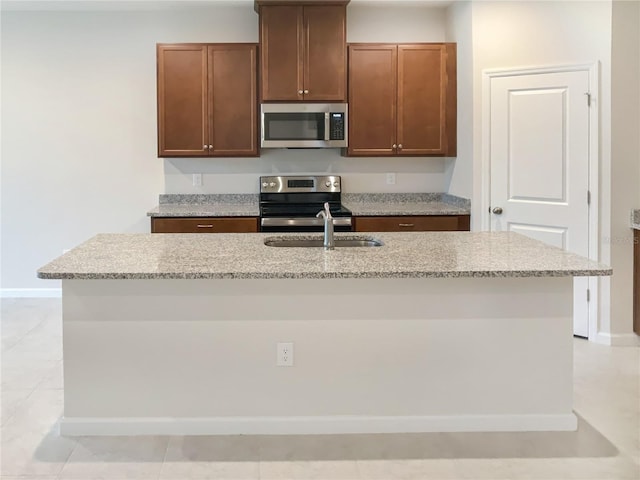 kitchen featuring a center island with sink, baseboards, appliances with stainless steel finishes, light stone counters, and a sink