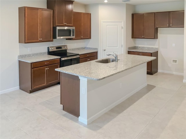 kitchen featuring a center island with sink, baseboards, light stone countertops, stainless steel appliances, and a sink