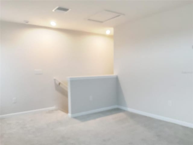 empty room with visible vents, light colored carpet, attic access, and baseboards