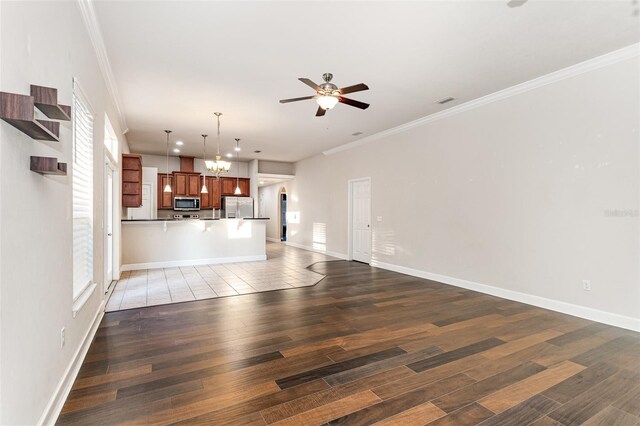 unfurnished living room featuring crown molding, baseboards, wood finished floors, and ceiling fan with notable chandelier