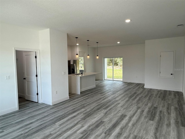 unfurnished living room with wood finished floors, recessed lighting, a sink, and baseboards