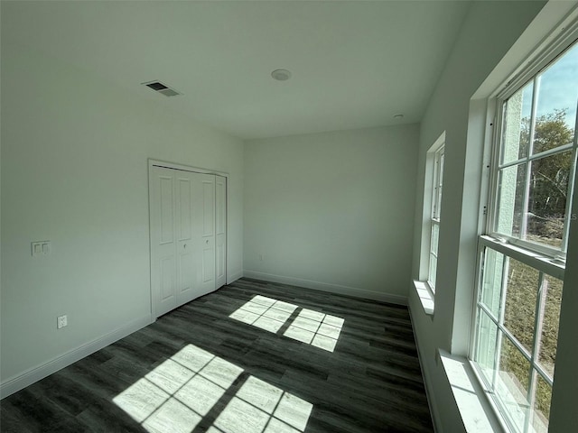 empty room with dark wood-type flooring, visible vents, and baseboards