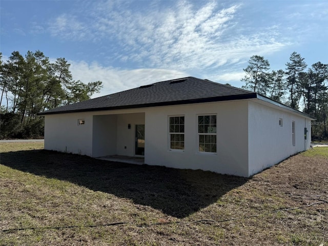 rear view of house featuring roof with shingles, a lawn, a patio area, and stucco siding