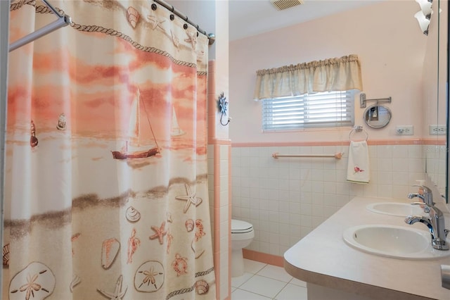 bathroom with a wainscoted wall, a sink, tile walls, and tile patterned floors