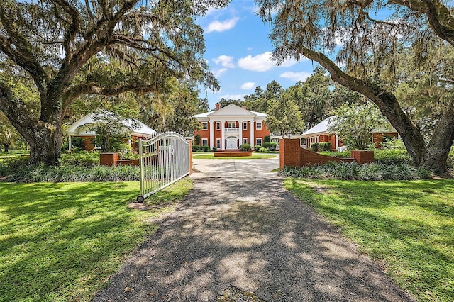 neoclassical / greek revival house featuring driveway, a front lawn, a fenced front yard, and a gate