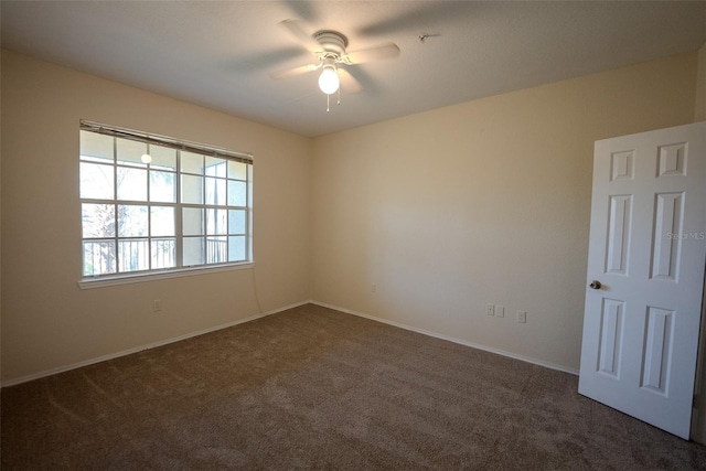 empty room with a ceiling fan, dark carpet, and baseboards