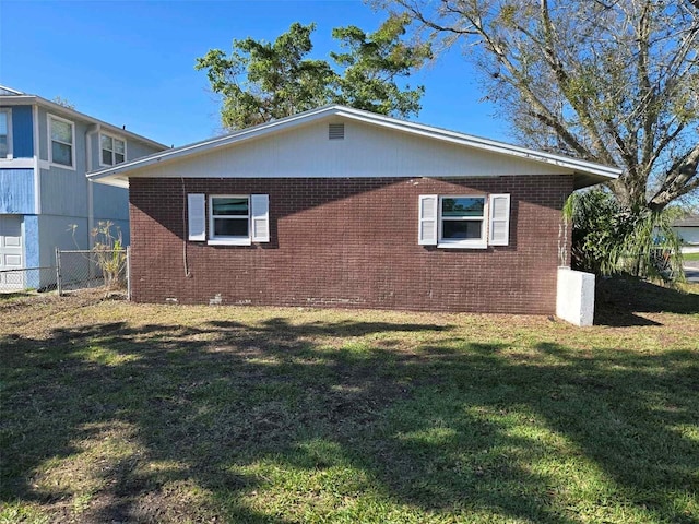 view of side of home with a yard, brick siding, and fence