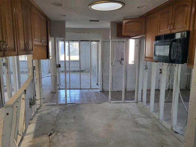 kitchen featuring brown cabinetry, black microwave, visible vents, and a textured ceiling