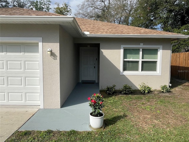 entrance to property with a garage, roof with shingles, fence, and stucco siding