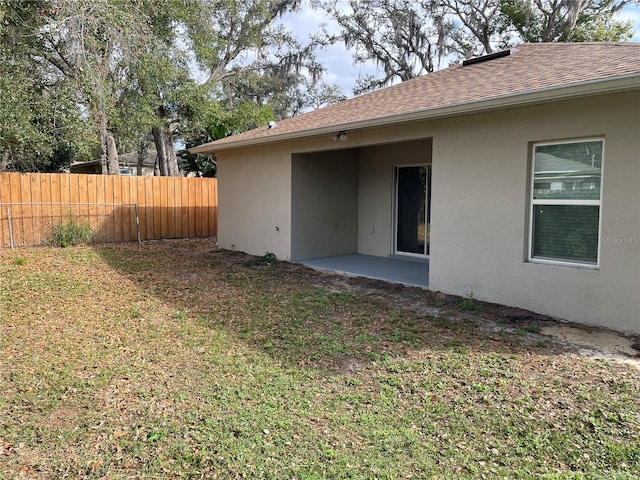 exterior space with a yard, a patio, stucco siding, a shingled roof, and fence