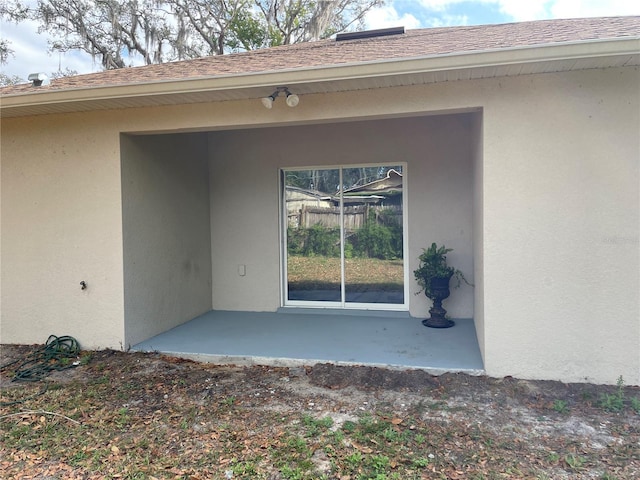 entrance to property with a patio, a shingled roof, and stucco siding