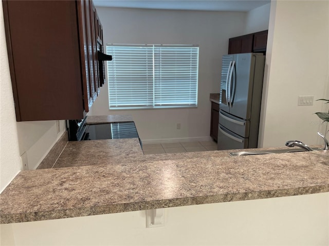 kitchen featuring light tile patterned flooring, a sink, baseboards, dark brown cabinets, and stainless steel refrigerator with ice dispenser