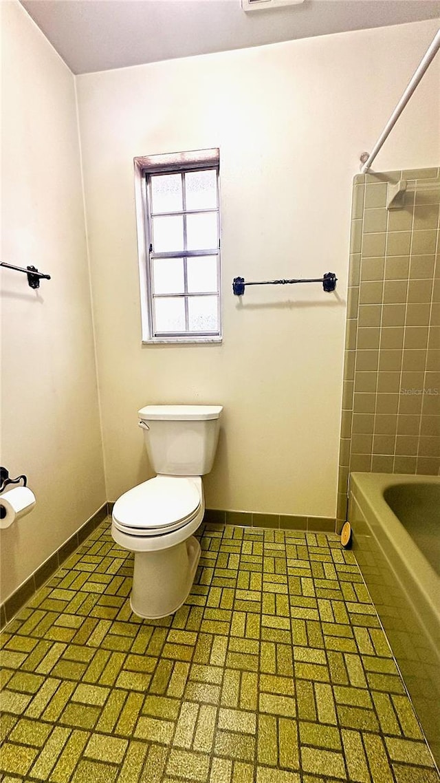 bathroom with brick floor, toilet, and baseboards