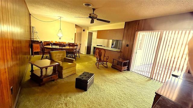 living area with carpet floors, visible vents, a ceiling fan, wooden walls, and a textured ceiling