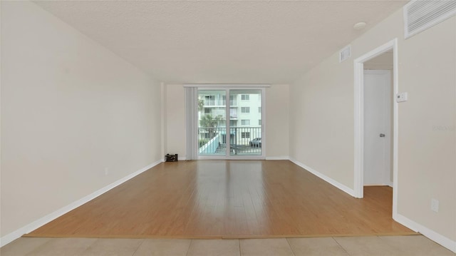 empty room with light wood-style floors, baseboards, visible vents, and a textured ceiling