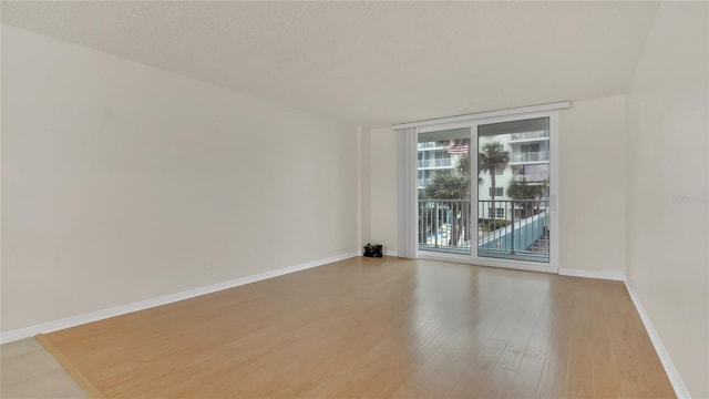 spare room with a wall of windows, a textured ceiling, baseboards, and wood finished floors