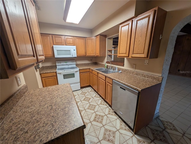 kitchen featuring arched walkways, white appliances, brown cabinets, and a sink