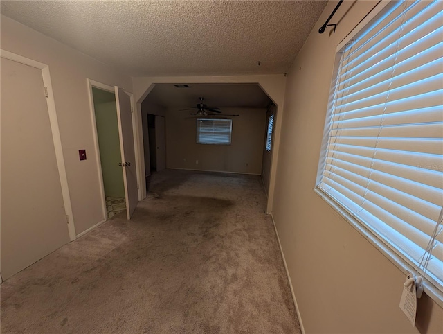 hall featuring a textured ceiling, arched walkways, visible vents, and light colored carpet