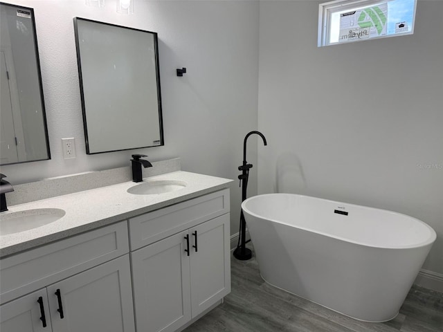 full bathroom with wood finished floors, double vanity, a freestanding tub, and a sink