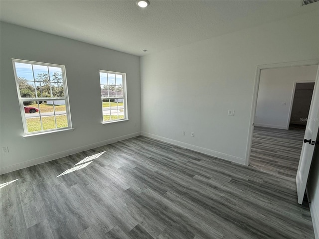 spare room featuring a textured ceiling, dark wood-style flooring, visible vents, and baseboards