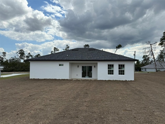 back of house with a shingled roof and stucco siding