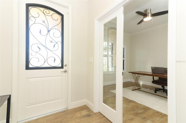 doorway featuring ornamental molding, ceiling fan, light wood-style flooring, and baseboards