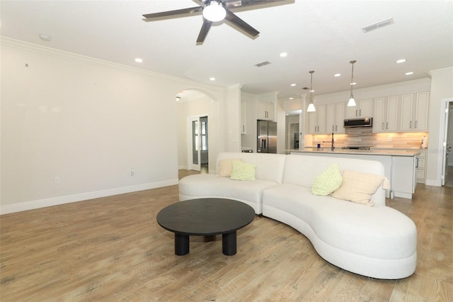 living area featuring arched walkways, visible vents, ornamental molding, light wood-style floors, and baseboards