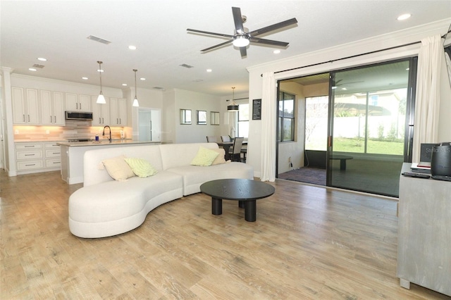 living room with light wood-type flooring, plenty of natural light, ornamental molding, and recessed lighting