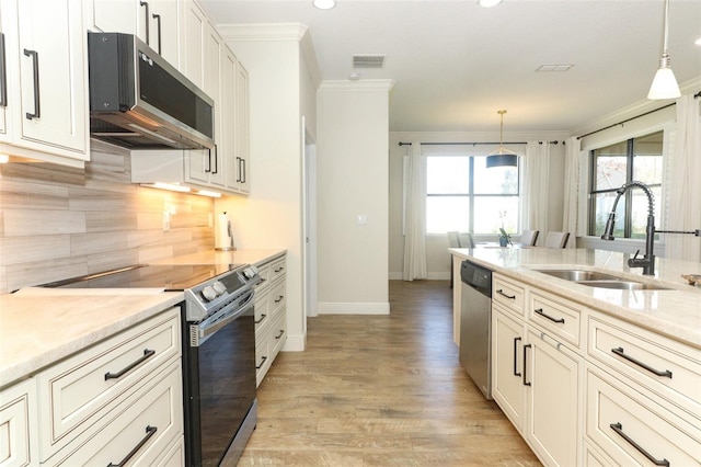 kitchen featuring light wood-style flooring, a sink, stainless steel appliances, crown molding, and backsplash