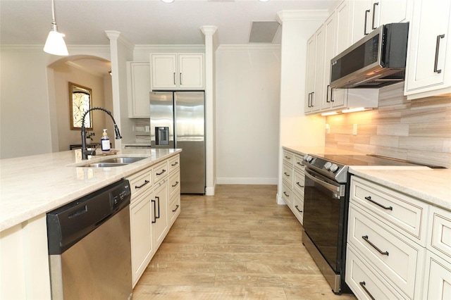 kitchen featuring arched walkways, appliances with stainless steel finishes, decorative light fixtures, crown molding, and a sink