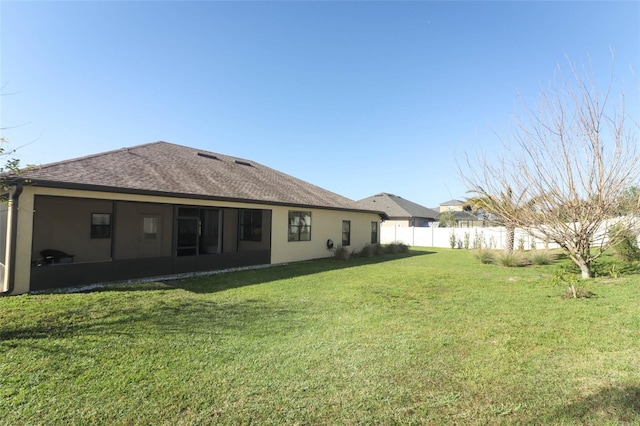 rear view of property featuring roof with shingles, stucco siding, a yard, and fence