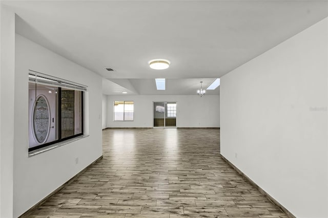 spare room with light wood-style flooring, visible vents, a chandelier, and baseboards