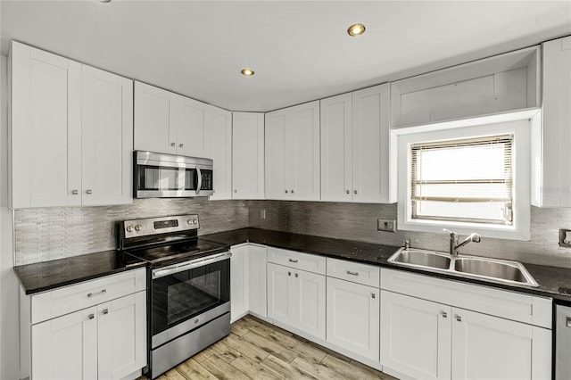 kitchen with appliances with stainless steel finishes, dark countertops, white cabinetry, and a sink