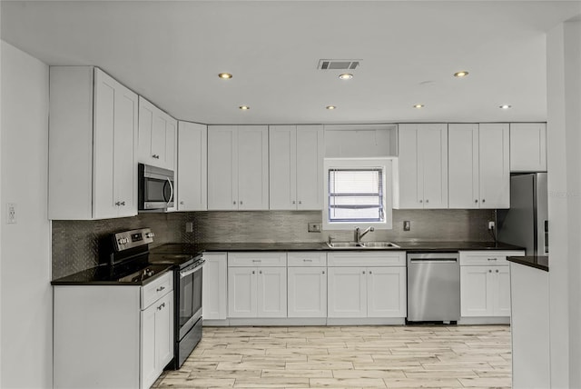 kitchen with visible vents, dark countertops, stainless steel appliances, white cabinetry, and a sink