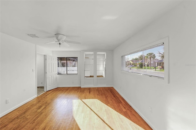 empty room with a ceiling fan, visible vents, baseboards, and wood finished floors