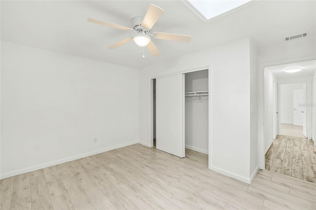 unfurnished bedroom featuring a skylight, a closet, visible vents, light wood-style flooring, and baseboards