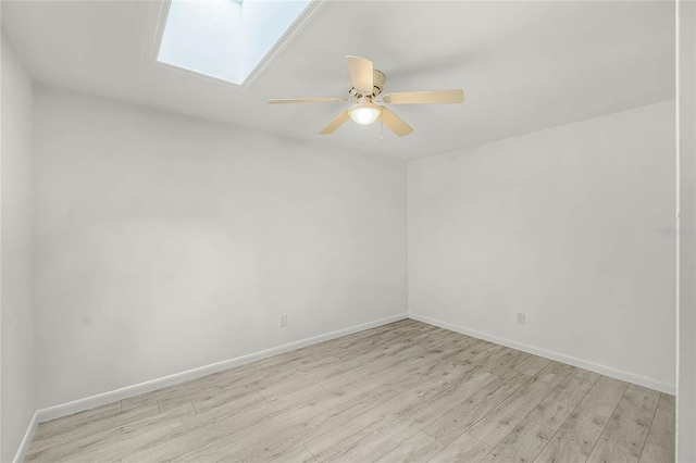 empty room with light wood-type flooring, a skylight, a ceiling fan, and baseboards