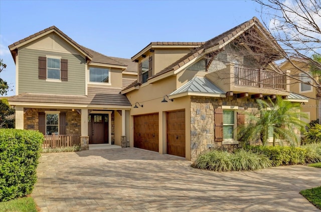 craftsman house featuring a balcony, stone siding, decorative driveway, stucco siding, and a standing seam roof