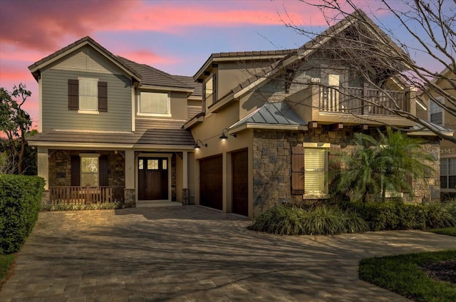 view of front of house featuring covered porch, a tile roof, stone siding, decorative driveway, and stucco siding