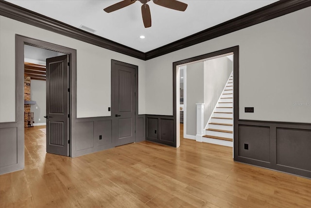 empty room featuring visible vents, a decorative wall, light wood-style flooring, stairway, and ornamental molding