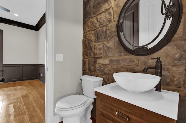 bathroom featuring toilet, a wainscoted wall, wood finished floors, vanity, and crown molding